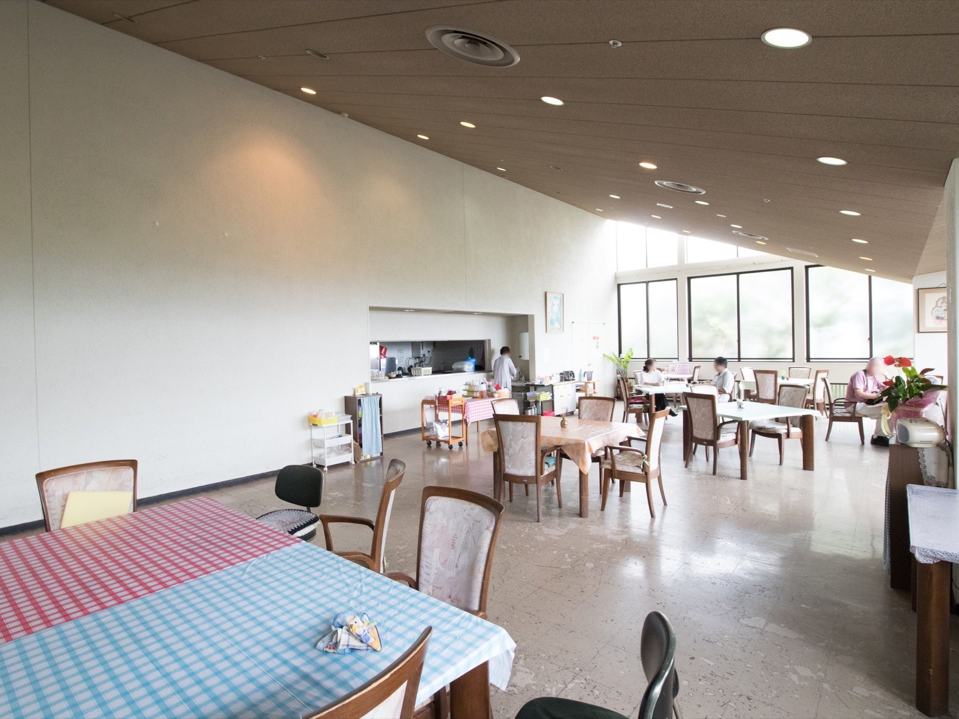 食堂は広々とした空間にゆったりと4人掛けテーブルセットが設置されている。数名の入居者様の姿が見える。