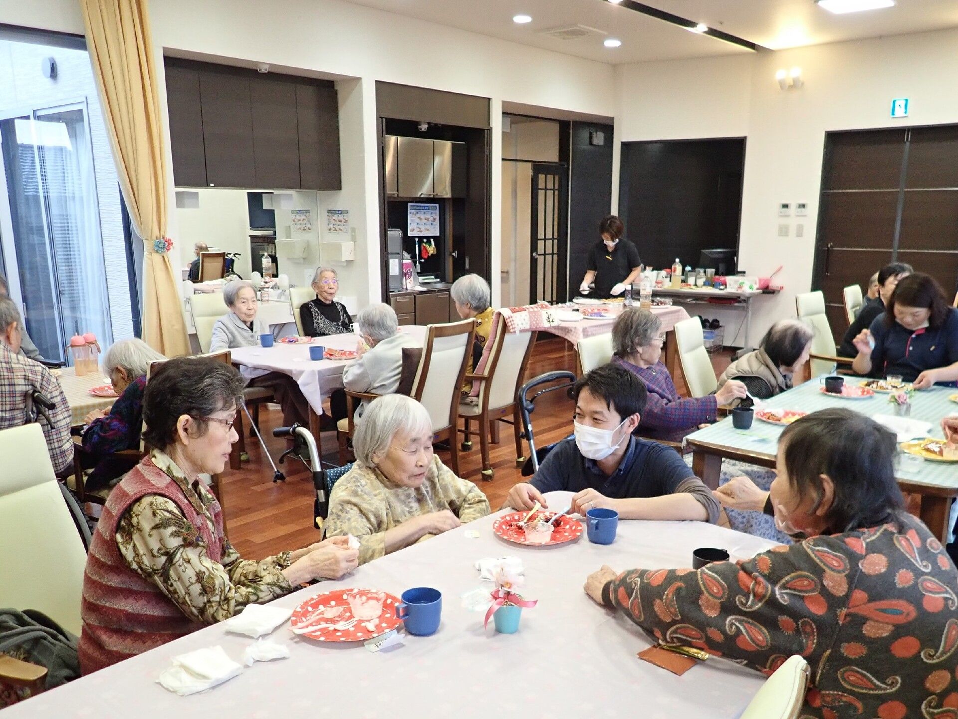 青いユニフォームを着た男性スタッフに教えてもらいながら体を動かしている高齢女性。二人とも同じポーズをしている。