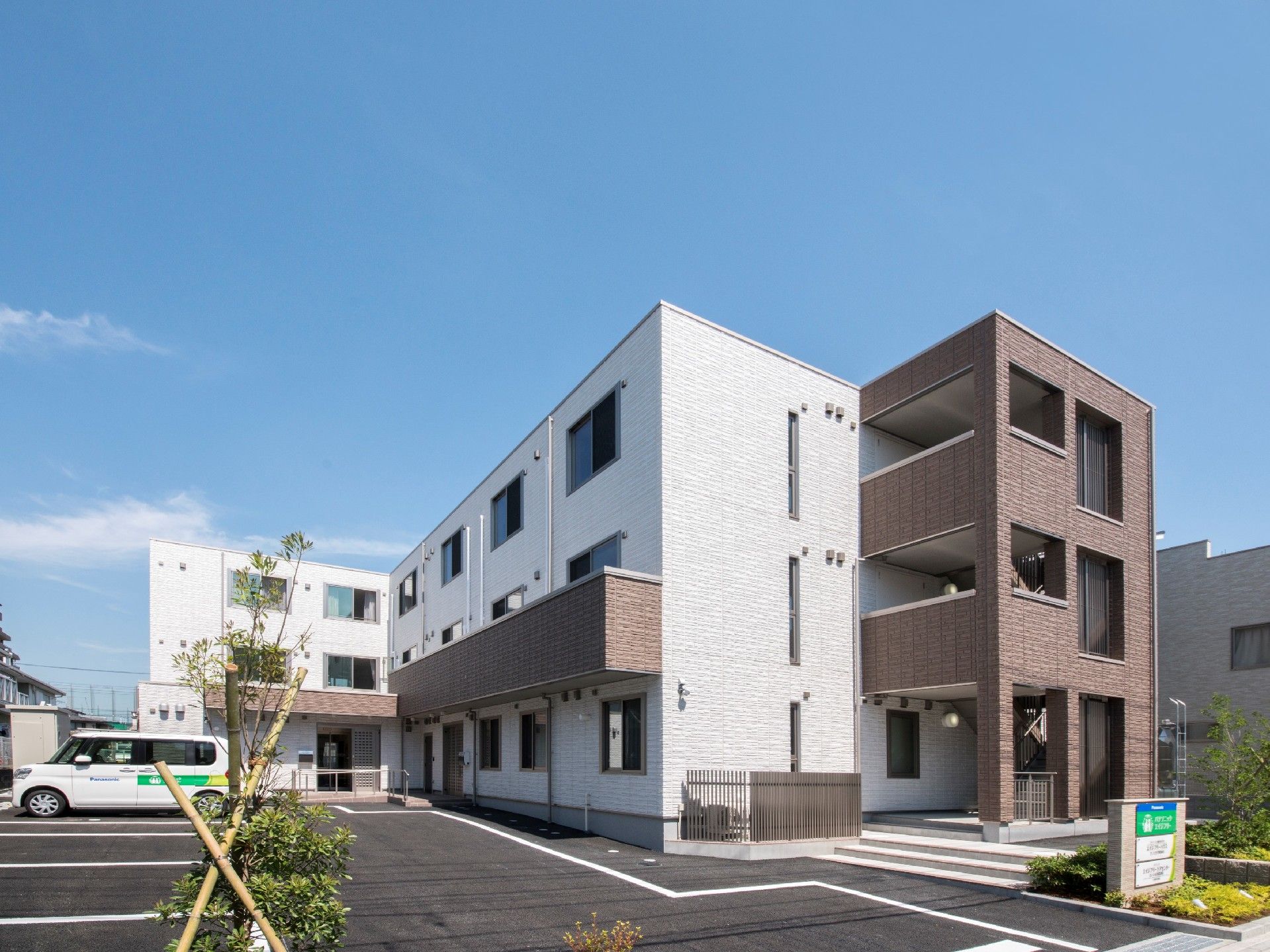 3階建ての建物は白とブラウンで屋外階段や駐車場もある。