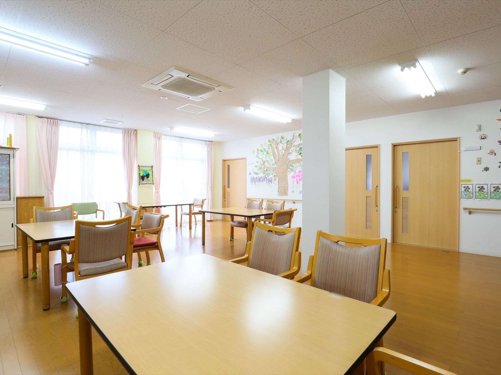 大きな窓があり、ゆとりをもったテーブル配置がなされた共有スペース。開放的で明るい室内となっている。