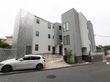 スタイリッシュな外観の建物。敷地内に自動車が1台駐車されており、その奧にステンレス製の手すりが連続しているスロープが見える。