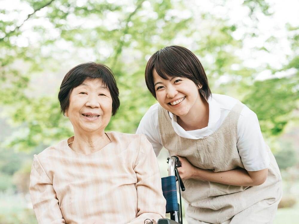 車椅子に座っている高齢女性と隣りに寄り添う女性ヘルパー