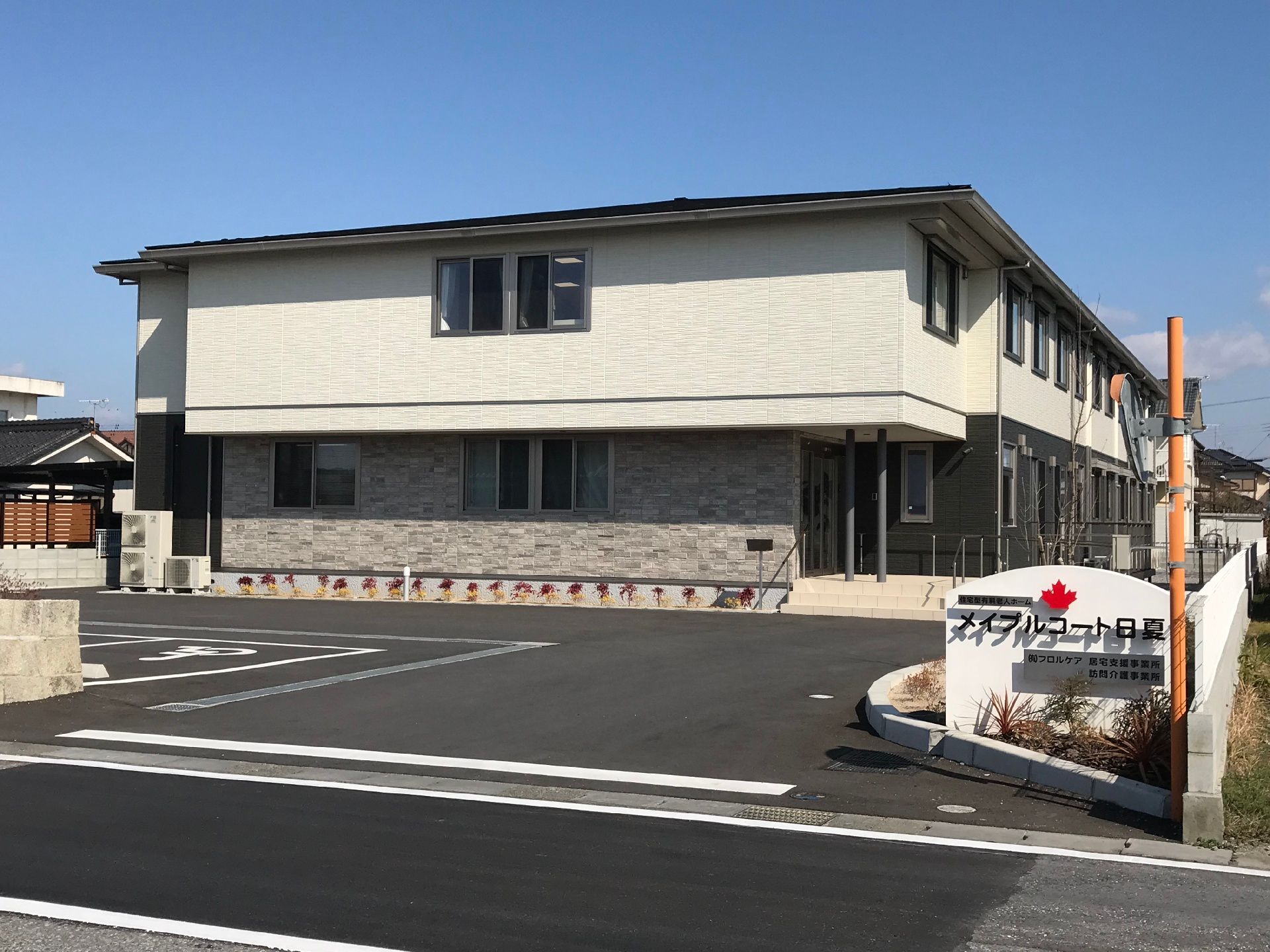 アイボリーの壁に黒い屋根の建てもの。入り口には施設名の書かれた看板が建っている