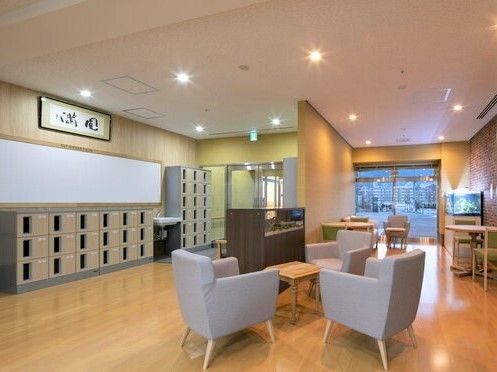エントランスを入ると個別の靴箱が置かれ、グレーの椅子が3脚テーブルを囲んで置かれ、奥にはソファやテーブルセットがある。