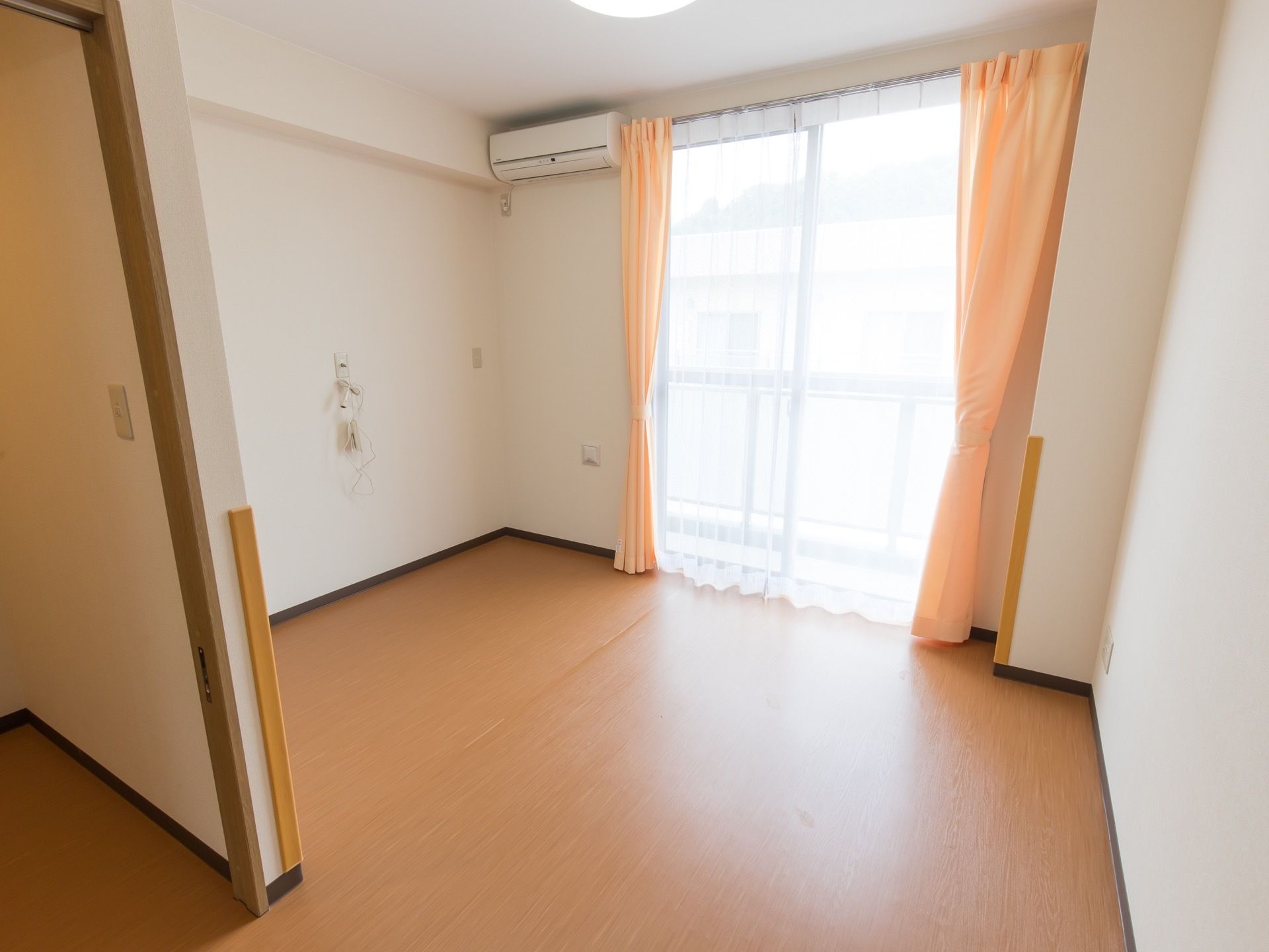 窓にカーテンが取り付けられており、左上方にエアコンが設置されている。左側の壁面にナースコールが取り付けてある。