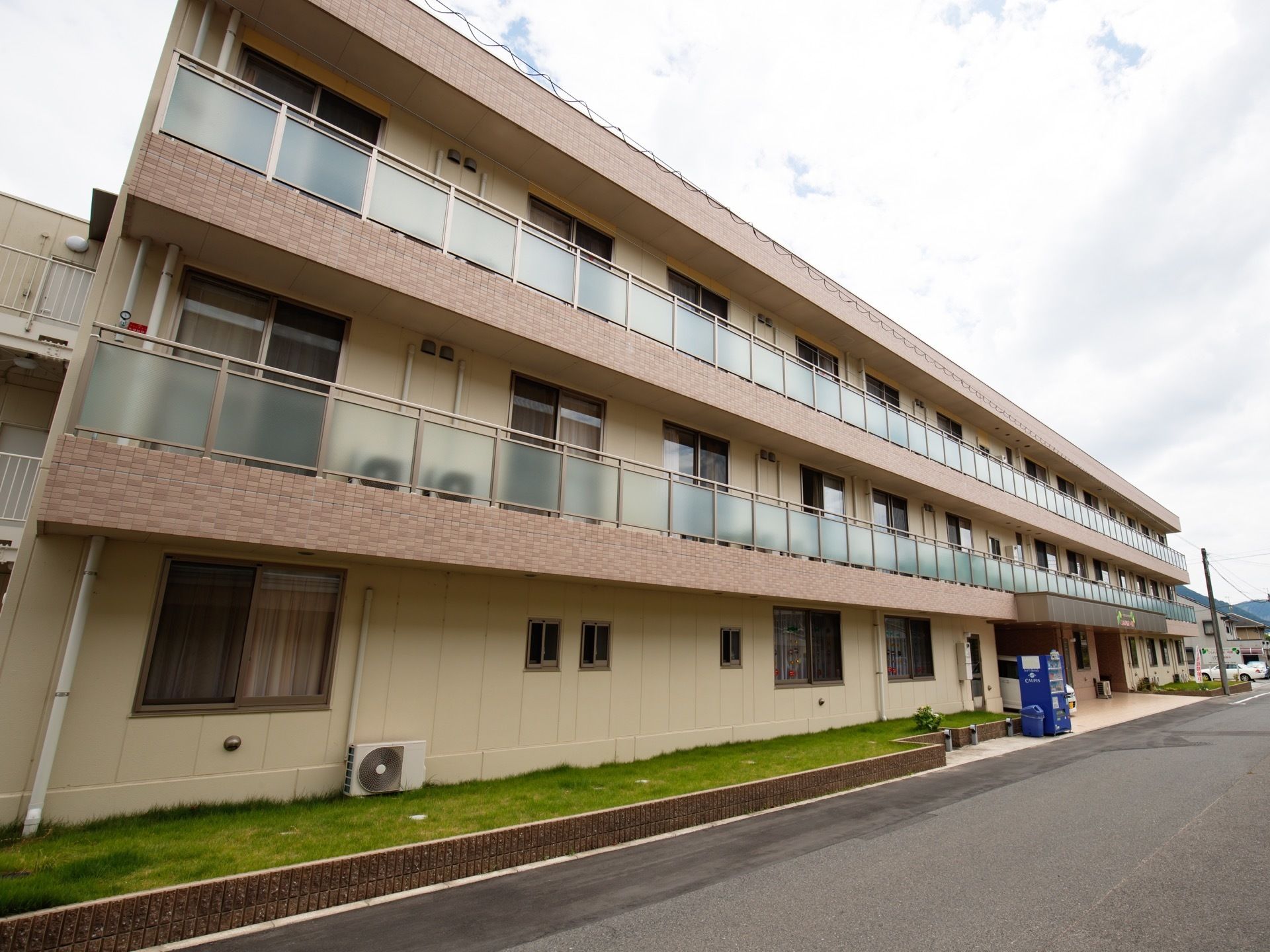 道路に面している横幅の広い３階建ての施設。建物の２階と３階部分にはベランダが設置されており、窓が並んでいる。