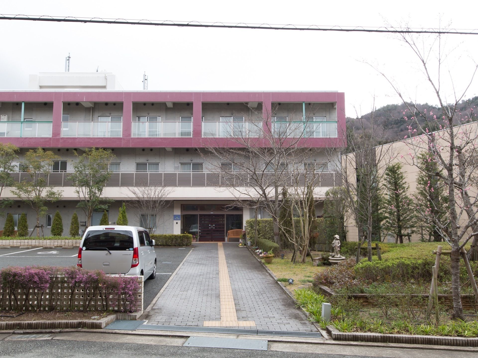 公道から玄関に向かって真っすぐに通路が伸びている。施設はコンクリート造りの３階建てである。通路の右側に桜などを植えた庭園がある。