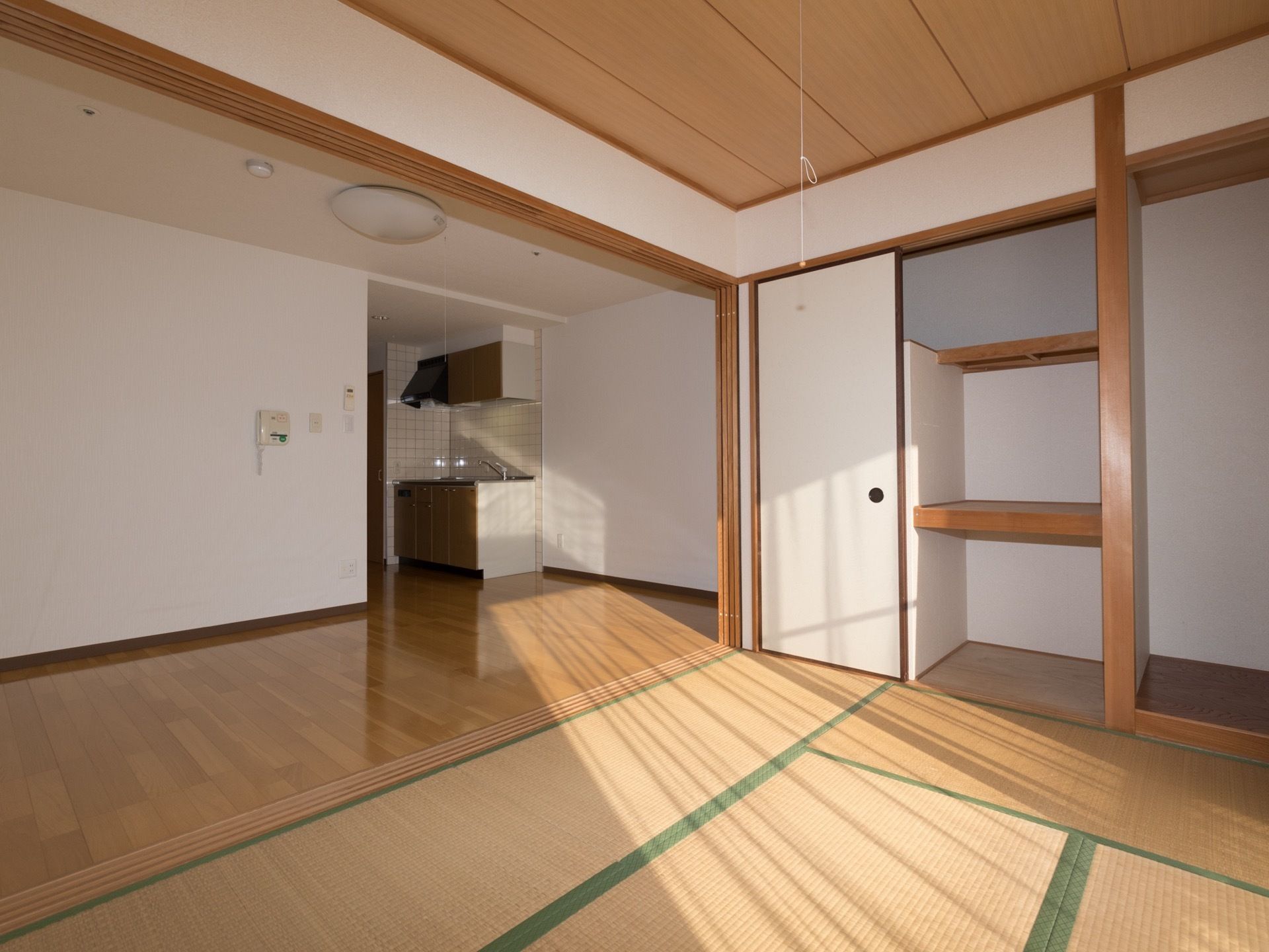 手前は和室で収納スペースが多くあり、奥は洋室になっている。部屋の奥にはキッチンがついている。窓から陽が差し込んでいる。