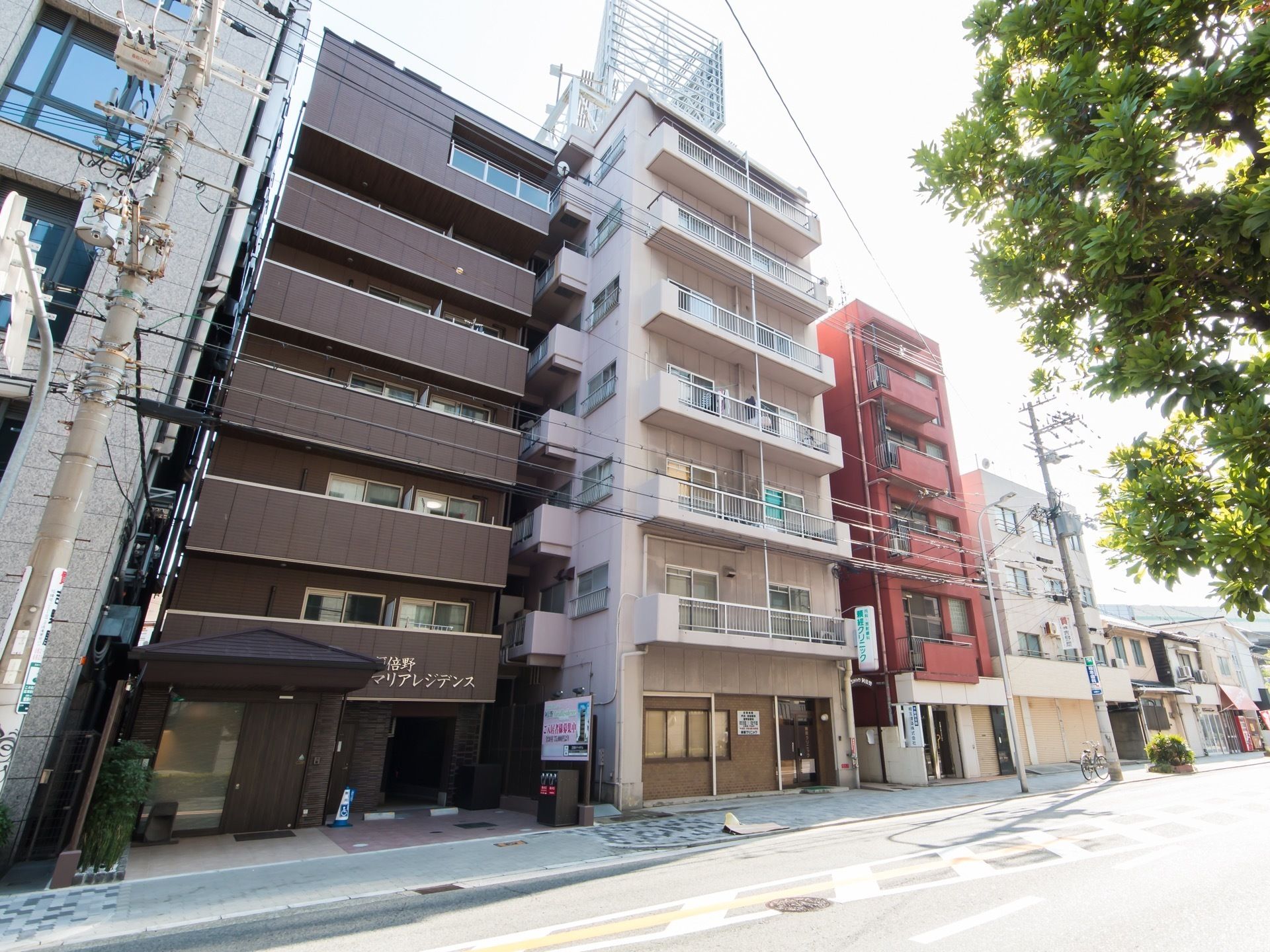 舗装された道路に沿って数件のマンションや民家が建ち並んでいる。電信柱から何本もの電線が張り巡らされている。