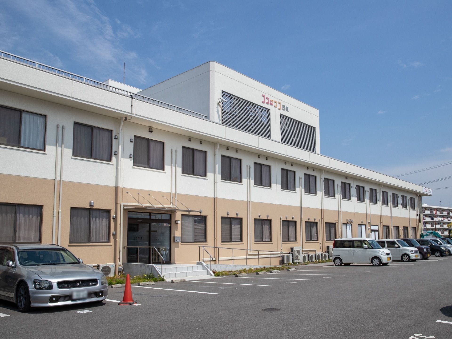 白と淡いピンクベージュのコントラストがモダンな２階建ての建物である。周辺はのどかで閑静な住宅街である。