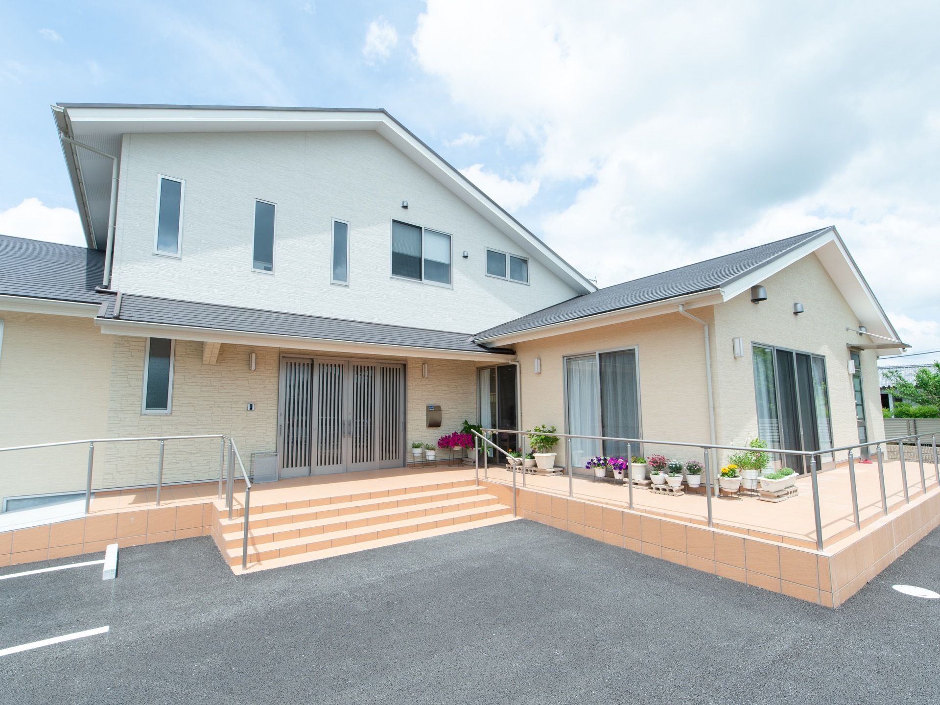 施設の建物の周囲の通路には手すりが設置されている。玄関前から建物の壁に沿って、草花の鉢やプランターが並んでいる。