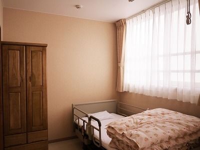 木製のクローゼットや寝具付きのベッドが置かれた居室には、カーテン付きの大きな窓が付き明るい。