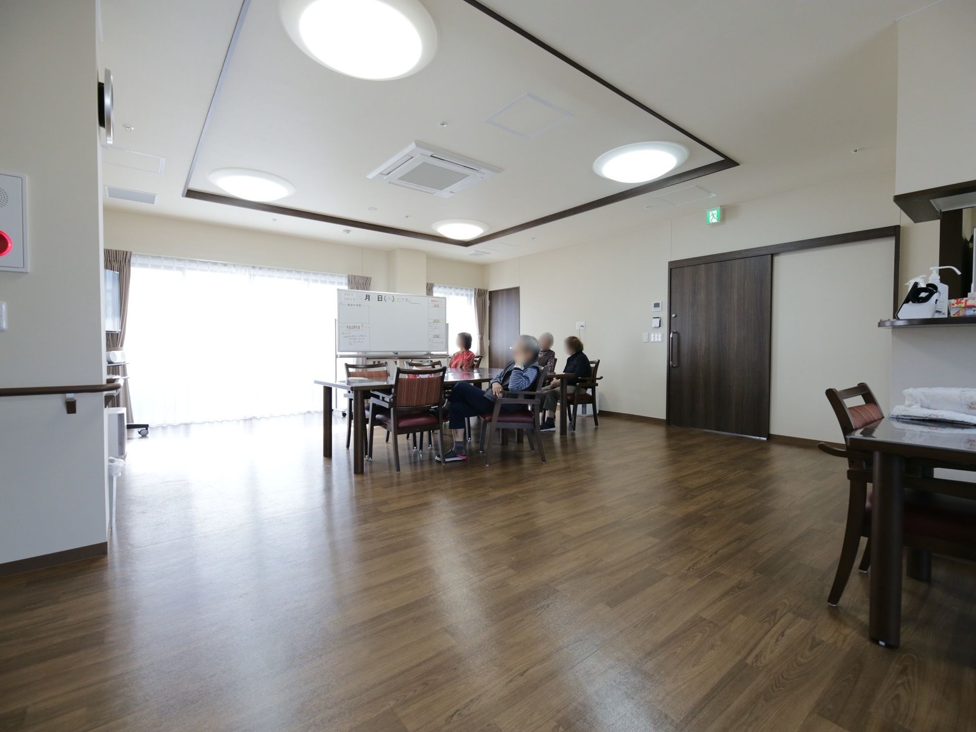 食堂は、クリーム色の壁紙にダークブラウンの建具と家具でまとめられている。天井には複数の照明があり、その中央にはエアコンが設置されている。