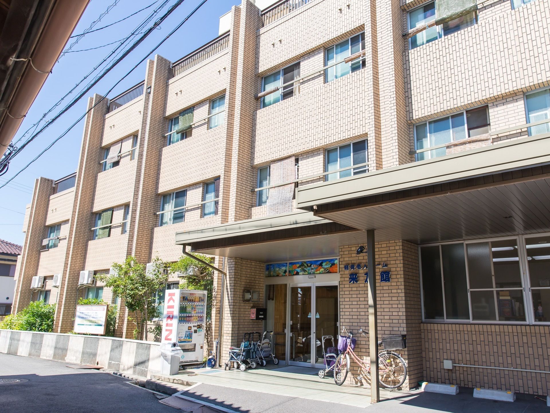 ブラウン色が基調の外壁になっている建物である。建物の前には自転車が置かれており、その隣には駐車スペースがある。