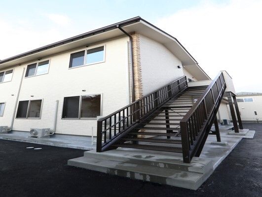 2階建ての建物はベージュ系でまとめられ、屋根が付いている。側面には屋外階段も設置されている。