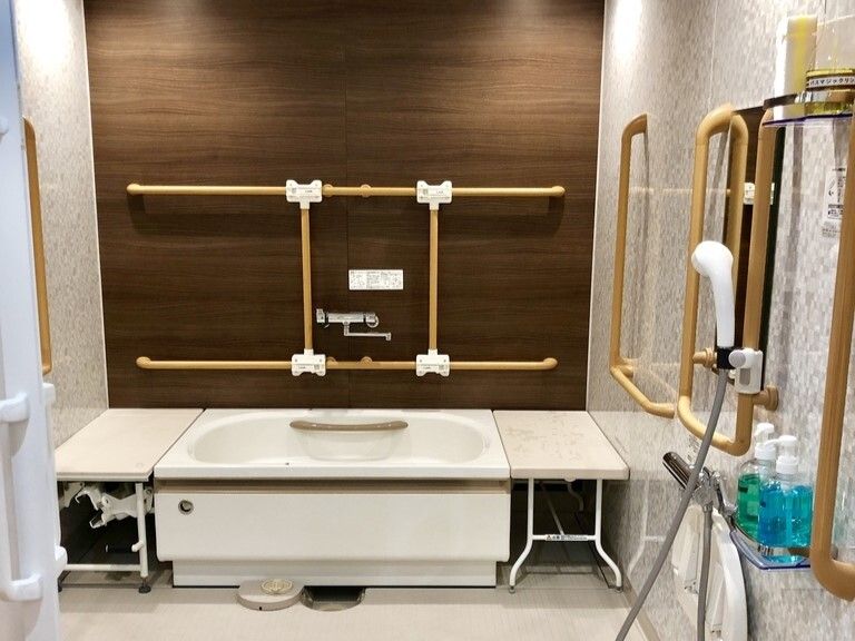 白を基調とした浴室には一人用の浴槽があり、ベージュの手すりが付き、浴槽の両サイドにベンチがある。