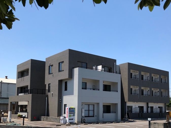 白とブラウンの3階建てで広い駐車場があり、日当たりのいい場所に建っている。