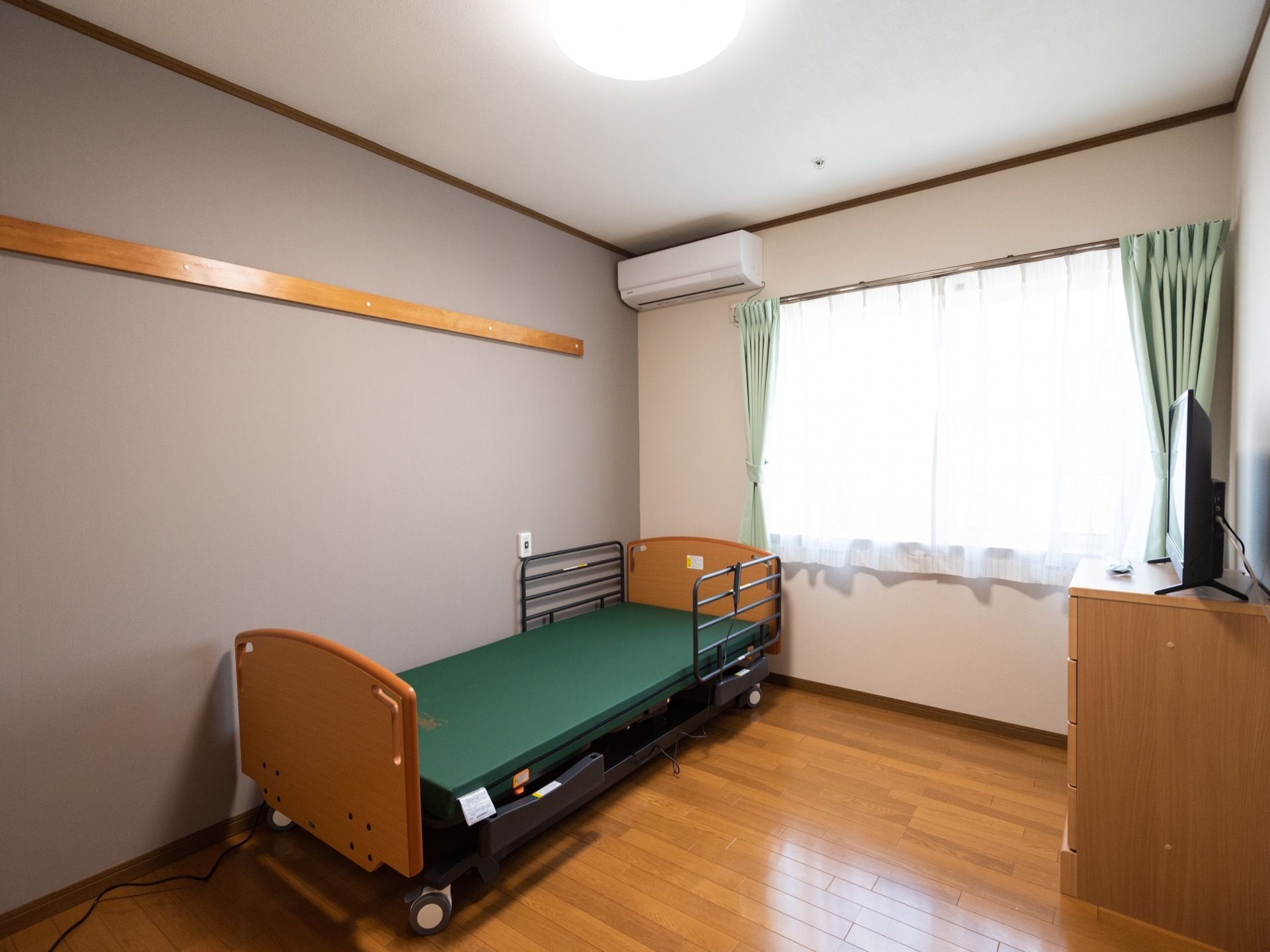 備え付けのベッドは電動式の介護用ベッドである。内装に合わせて頭と足のボード部分は木製である。壁には、なげしが設置されている。