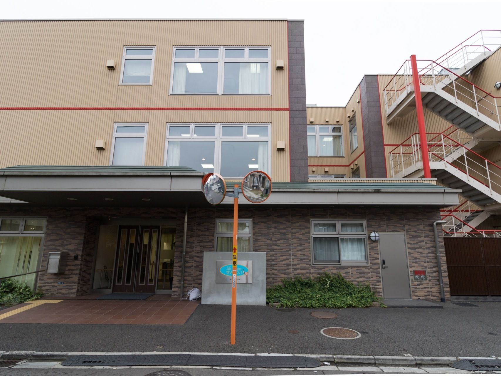 三階建ての建物が建っている。歩道から玄関までは段差のない造りになっている。屋上と地上を結ぶ外階段がある。