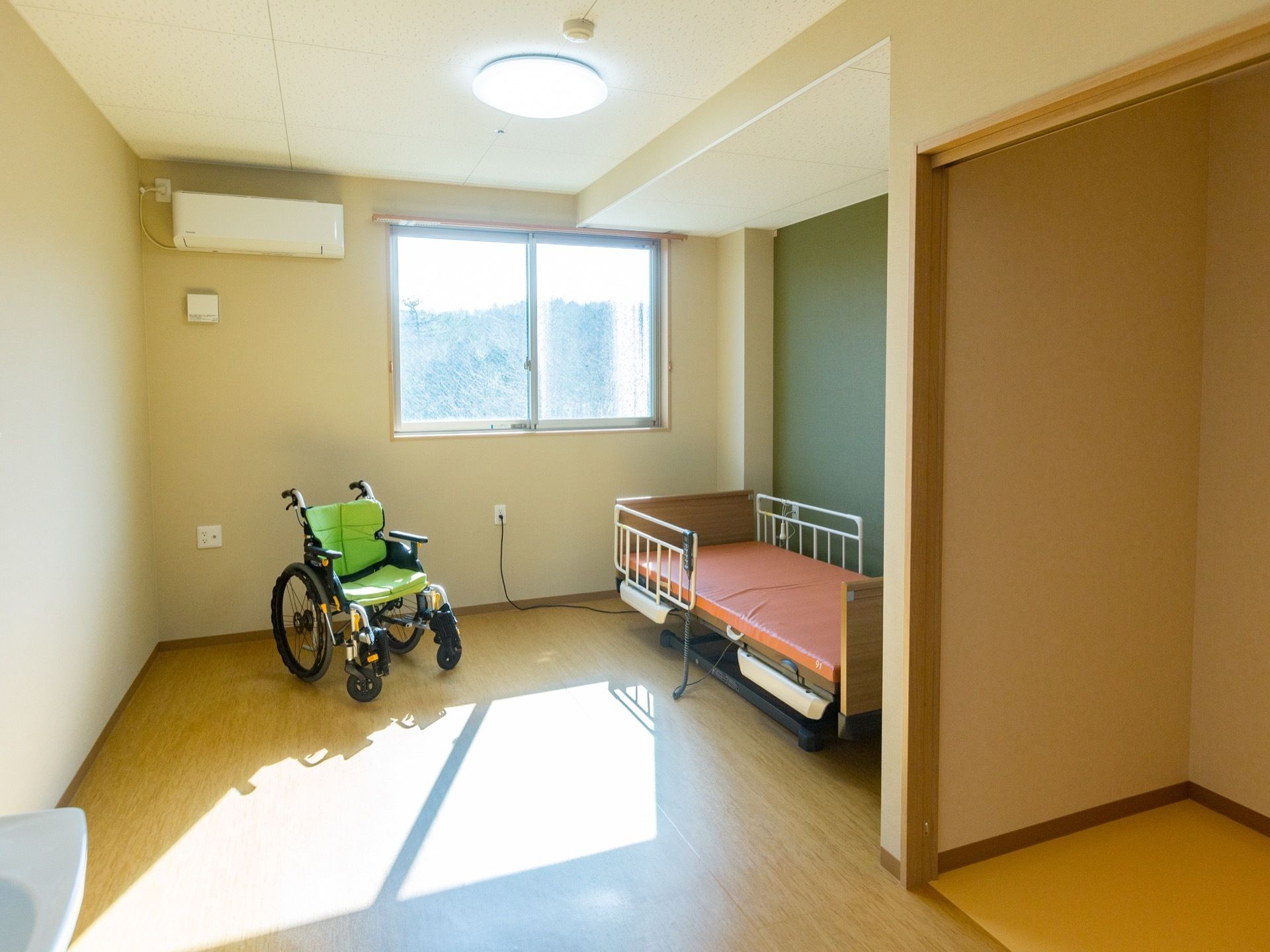 日当たりが良い個室の部屋である。ベッドが設置されており、車椅子が用意されている。エアコンが完備されている。