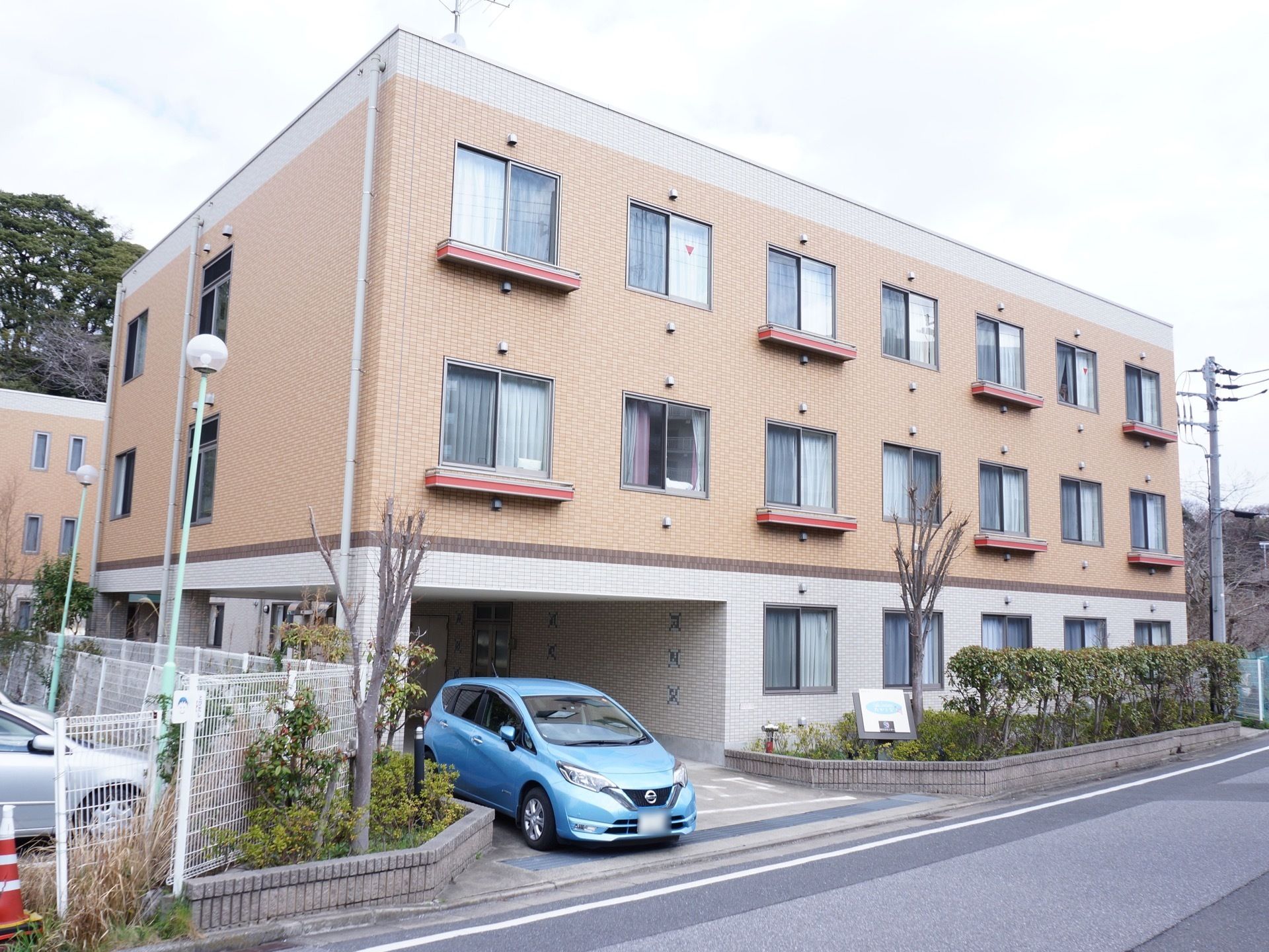 茶色が基調の外壁となっている３階建ての建物である。駐車場があり車での来訪も便利である。建物の周りに木々が植えられている。