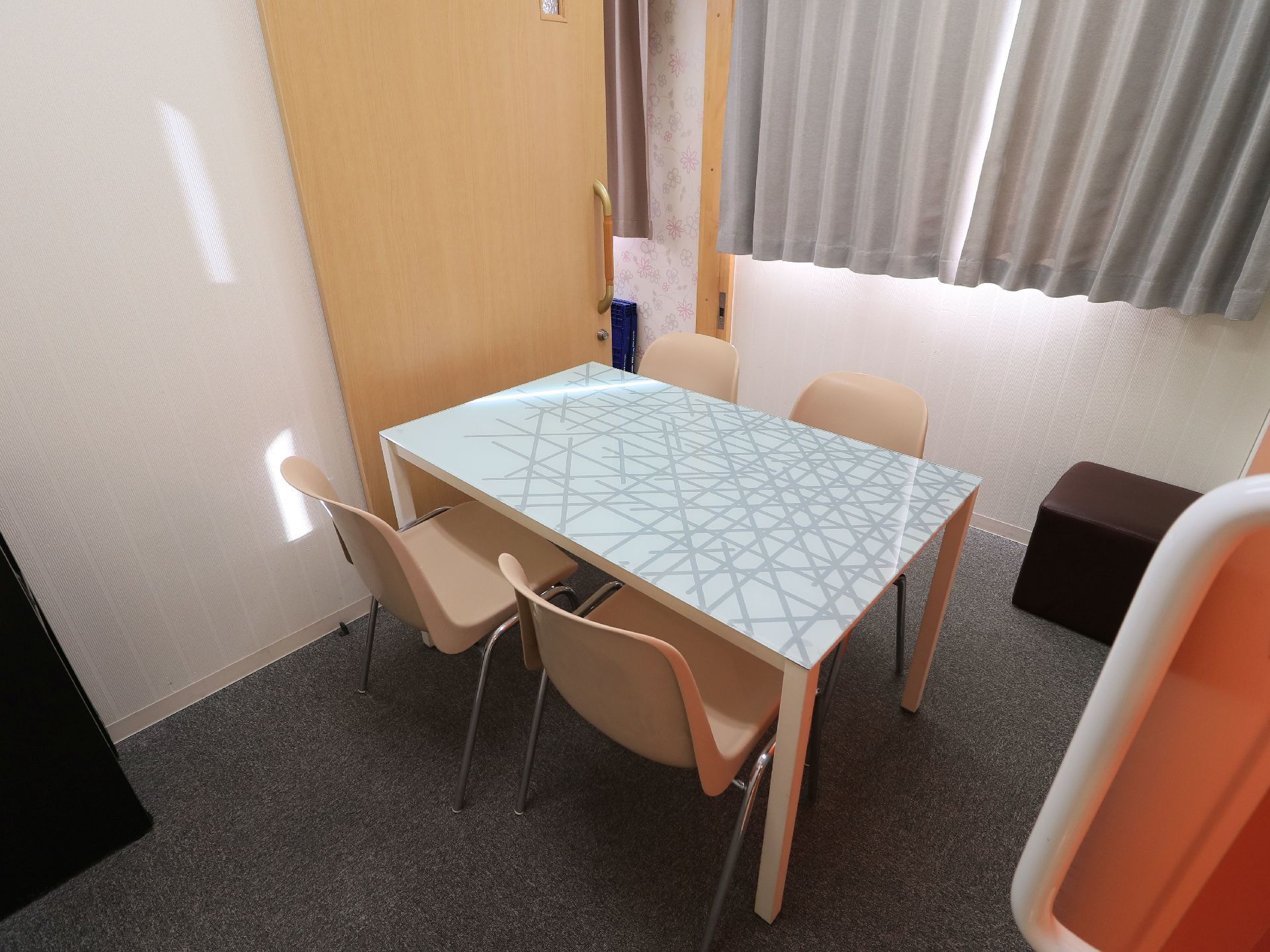 遮光カーテンが掛かったシンプルな相談室である。白に模様が入った天板のテーブルに椅子が4脚配置されている。