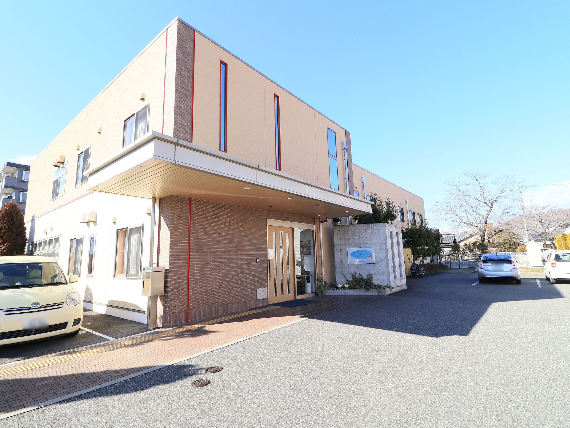 ブラウンとイエローベースの壁に赤のラインがオシャレな施設建物である。周辺の路面はフラットで開放的である。