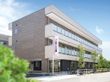 ベランダ付きの3階建ての建物。道路に面していて、周辺には花や木が植えられている。
