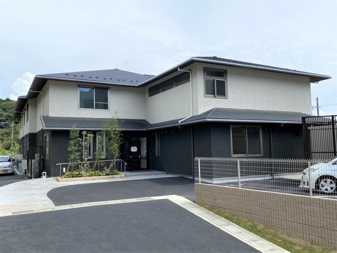 駐車場が付いた2階建ての建物。ダークグレーと白で和の雰囲気があり、三角の屋根が付いている。