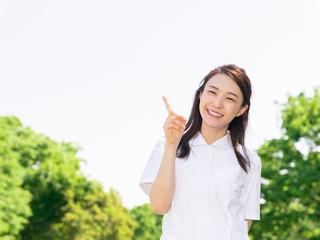 白衣を着た若い女性スタッフが笑顔で緑の多い屋外で過ごしている。