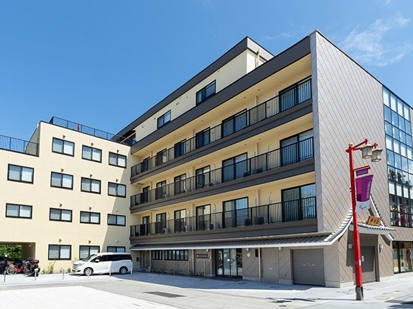 広い駐車スペースがある、ベージュ系の外壁の5階建て建築物