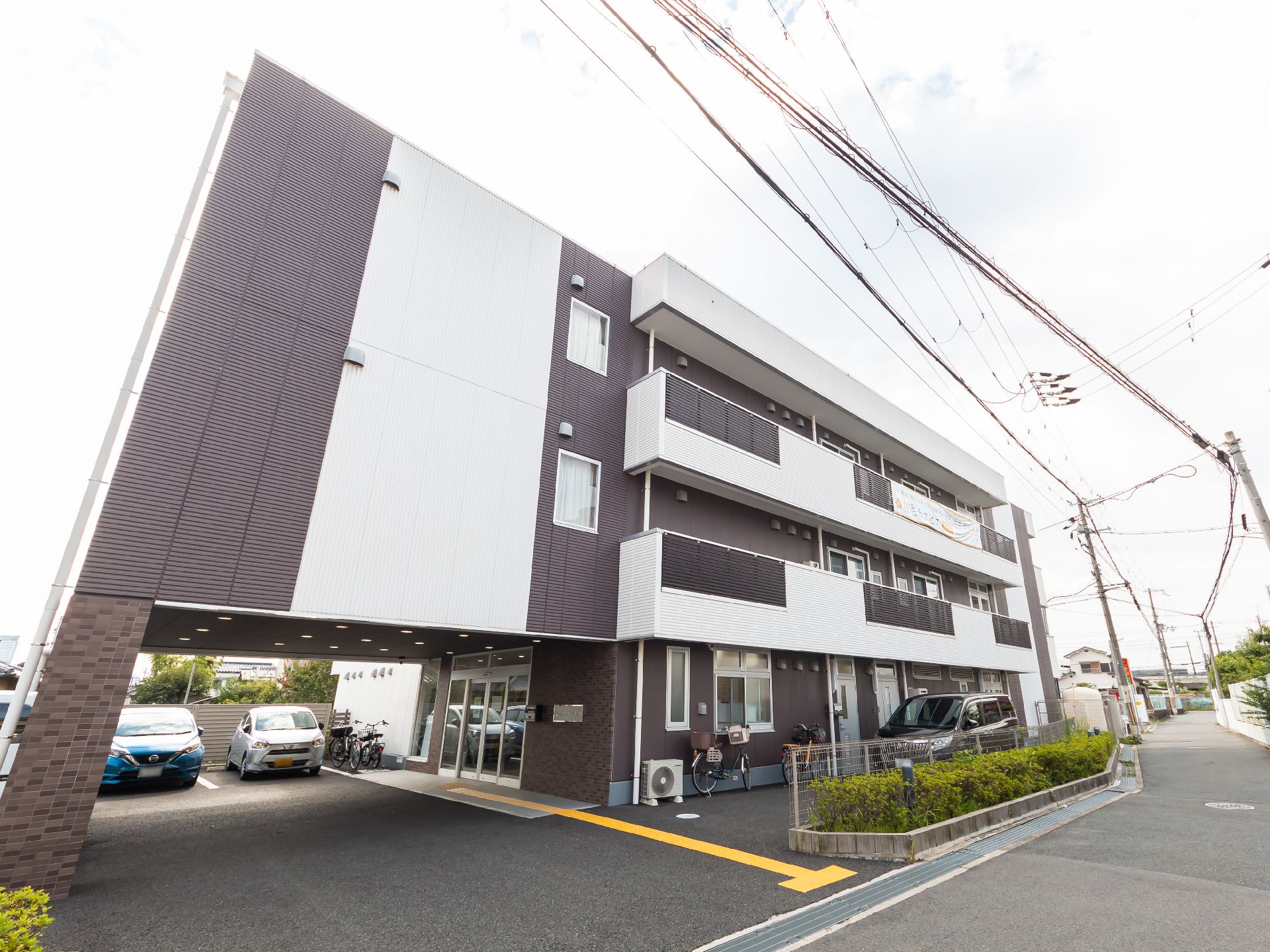 アスファルトの道路沿いに立地している白と黒の外観の３階建ての建物