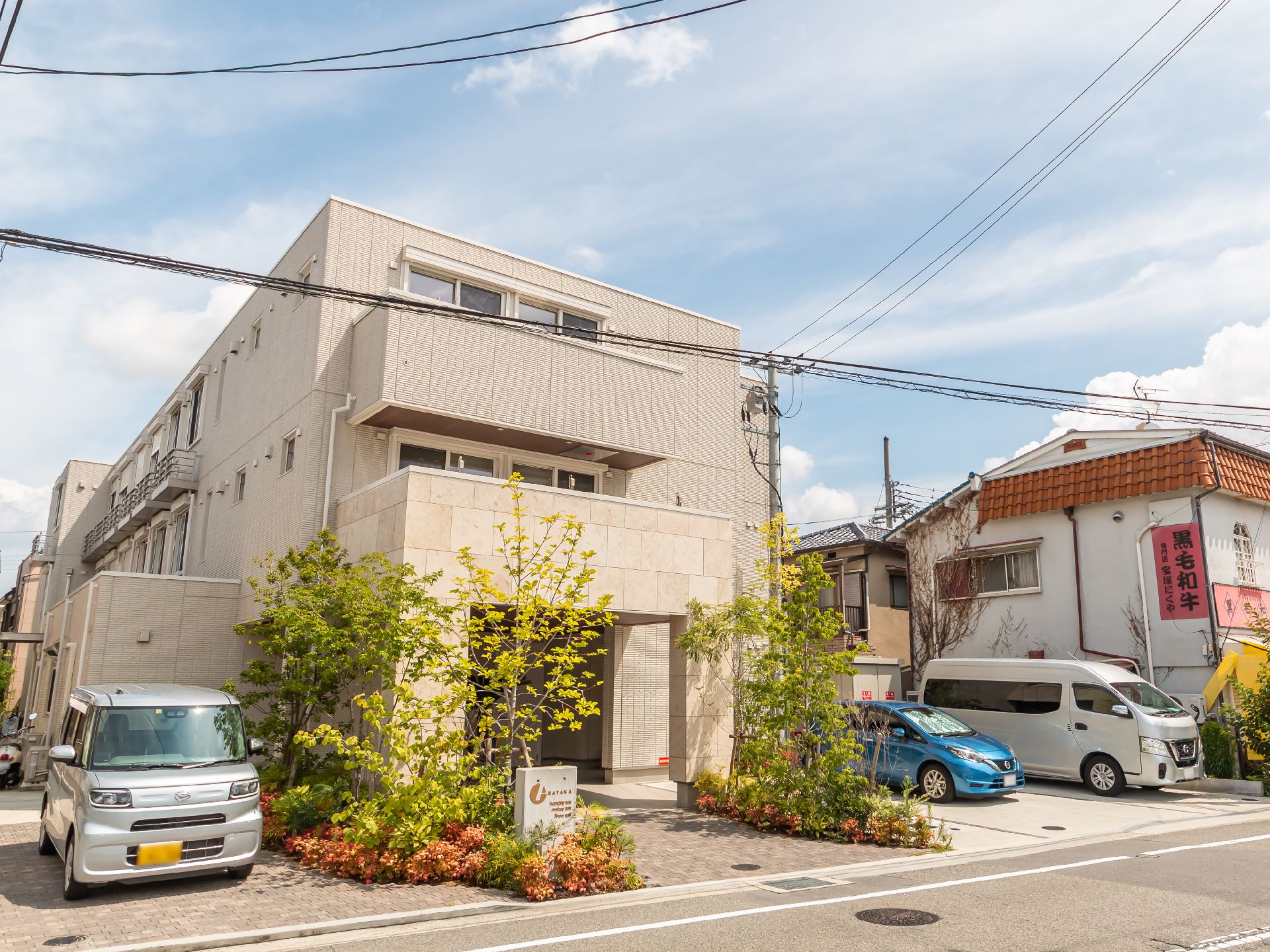 目の前に車が止まったベージュ系の外観で３階建ての建物