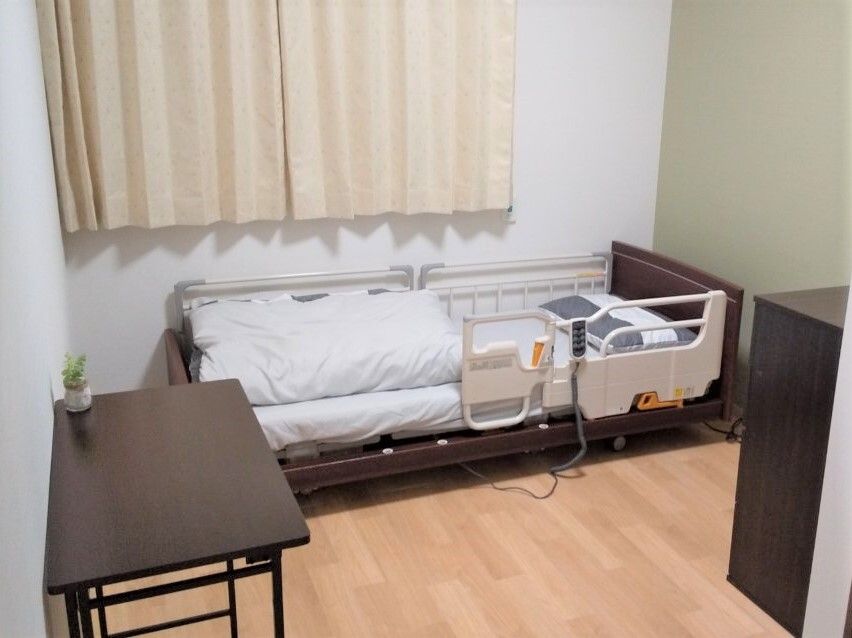 介護用ベッドとテーブル、タンスなどが並べられている施設内の個室の様子