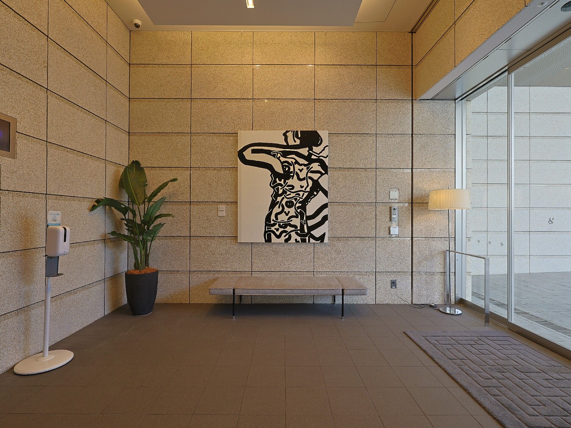 モノクロの大きな絵画が飾られたエントランスにはベンチや観葉植物があり、手すりも設置されている。