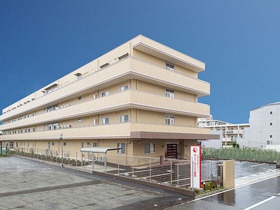 4階建ての建物の各フロアにベランダが付いている。ベージュ系の外壁で敷地内には駐車場があり、花壇もある。