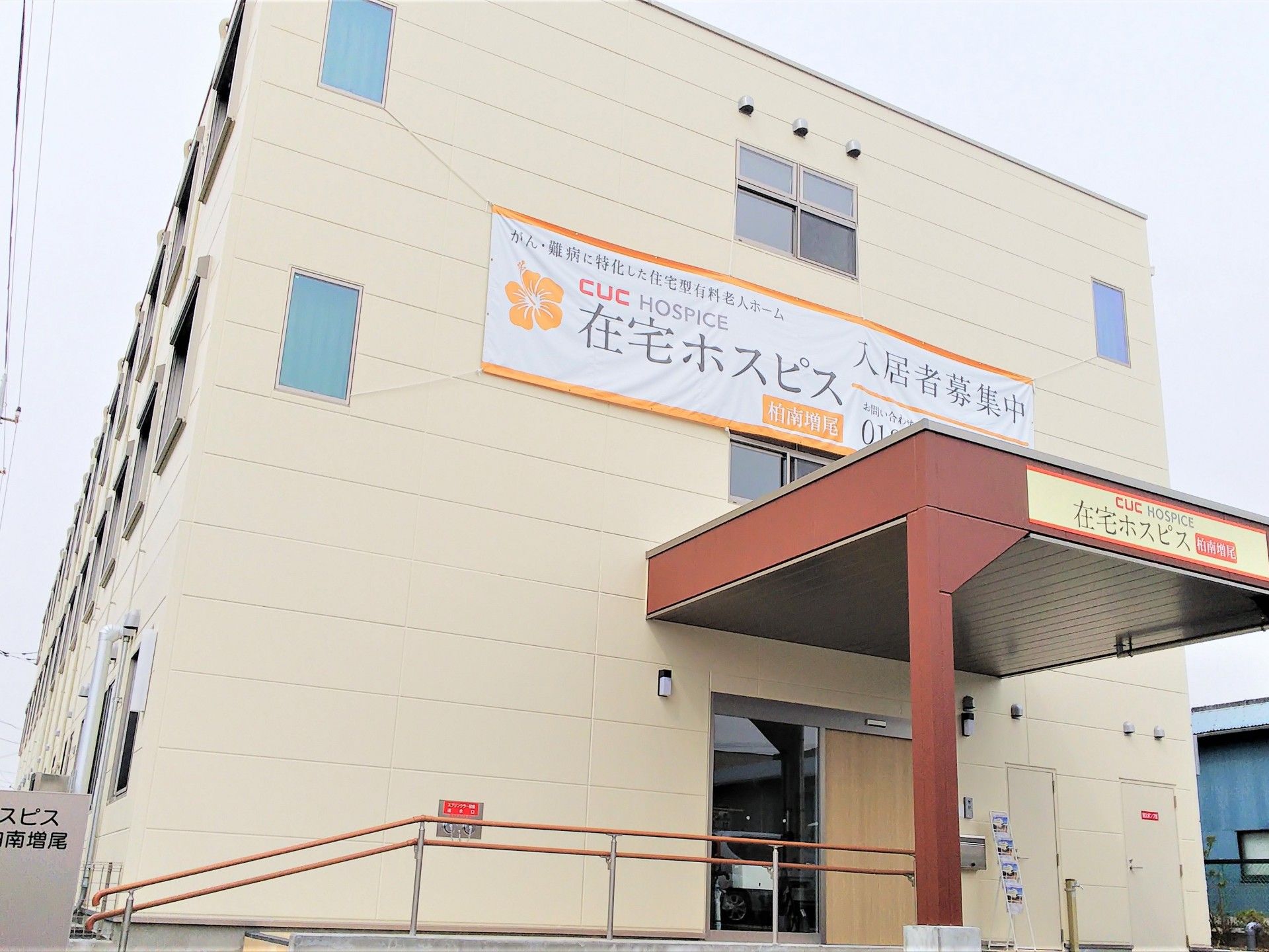 白を基調とした３階建ての建物。玄関先には屋根が付き、広い駐車場もあり、明るい雰囲気。