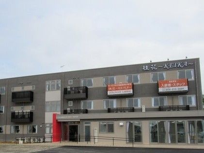 ３階建ての建物。ブラウンを基調とし、窓が多く、玄関には屋根が付き、手すり付きのスロープもある。