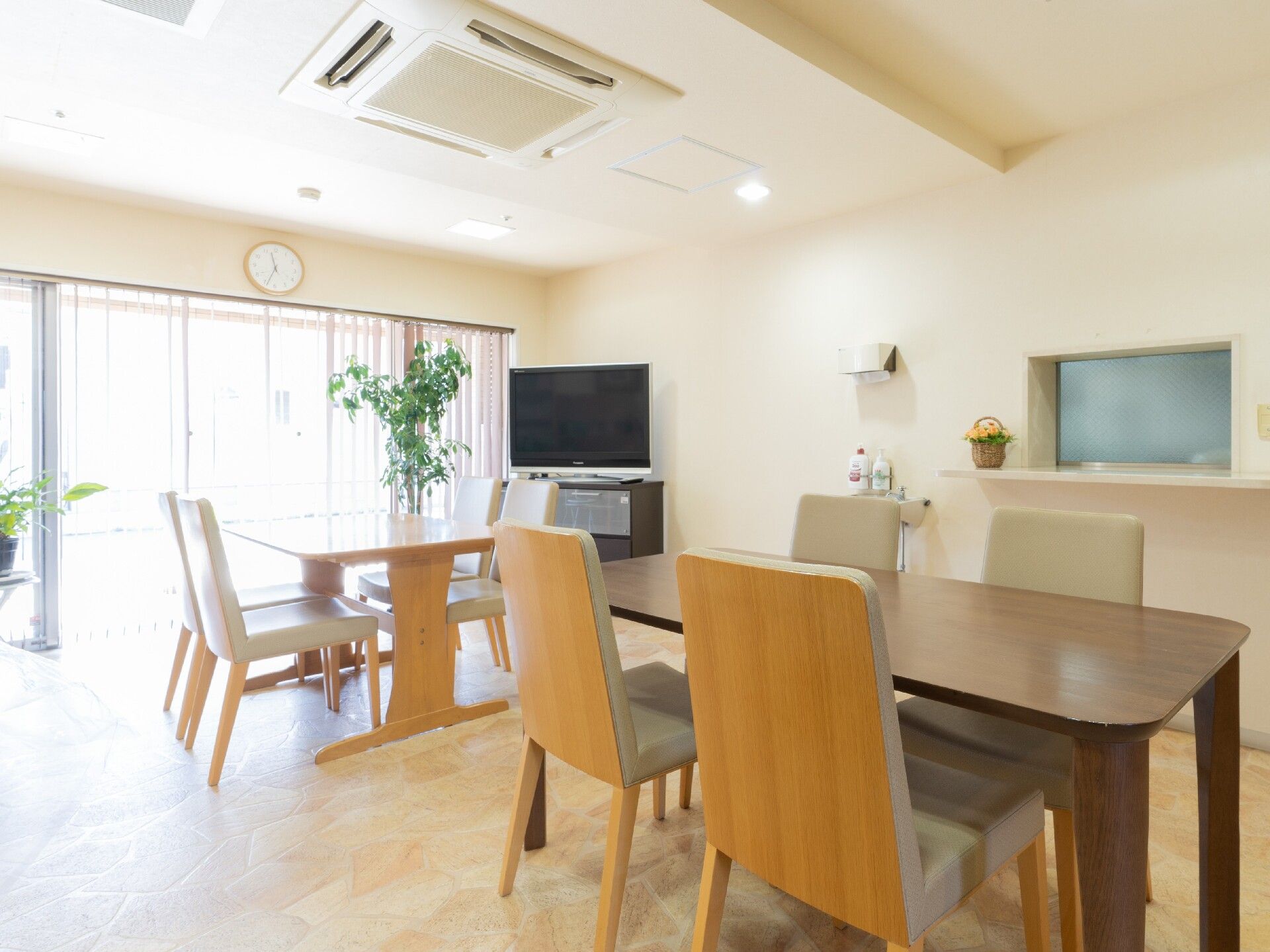 テレビや４名掛けのテーブルが設置された食堂の様子。窓から明るい光が射し込んでいる