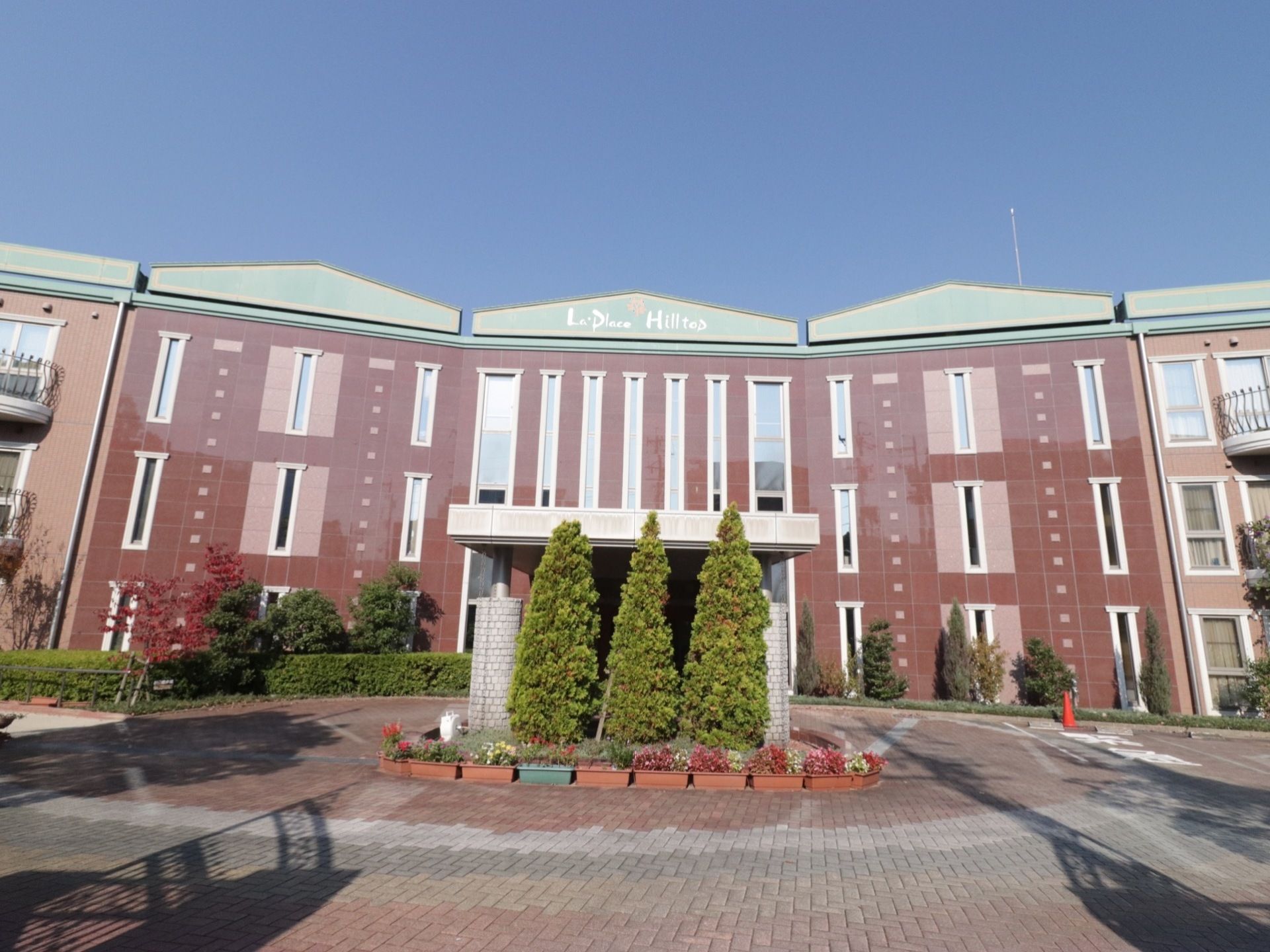 施設の建物は中庭を丸く囲むように建っており、どこかホテルのようなたたずまいである。中央の建物に入口があり、三角屋根に施設名が表示されている。