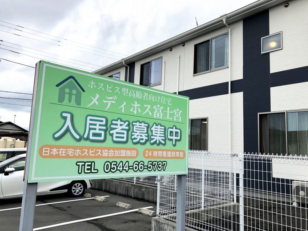 白と黒の外壁の２階建ての建物は横に長く、建物の前には看板があり、駐車場も付いている。