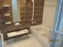 白とブラウンの一人用の浴槽が設置された浴室。壁には手すりがあり、浴槽内にベンチもある。