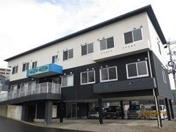 3階建ての建物の1階部分は駐車場となっていて、2階部分が黒、2階部分が白の外壁。窓がたくさん付いている。