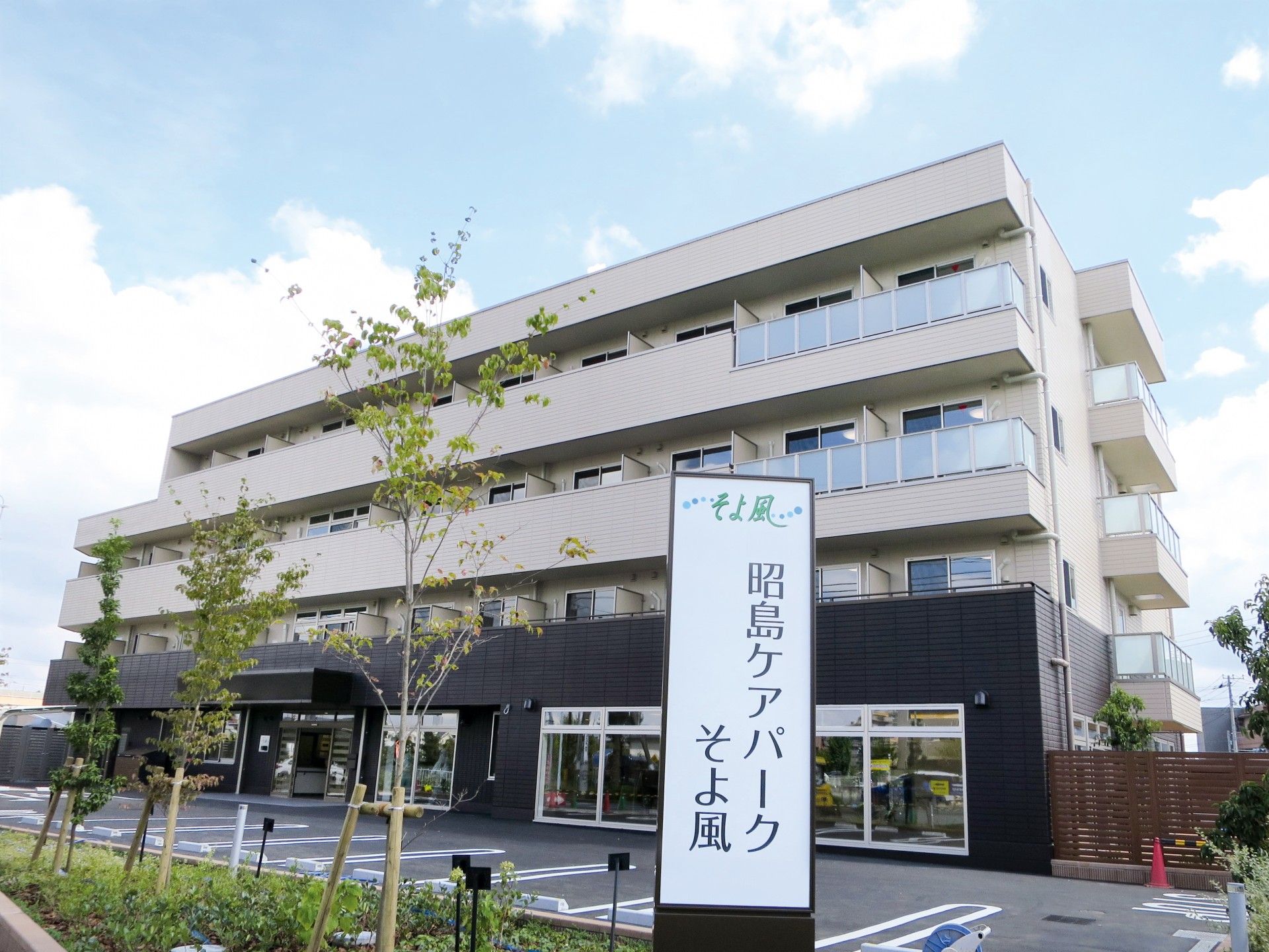 4階建ての建物の下の部分がダークブラウンで上の部分が白。周りには木が植えられ、ホーム名が書かれた看板が建っている。