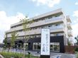 4階建ての建物の下の部分がダークブラウンで上の部分が白。周りには木が植えられ、ホーム名が書かれた看板が建っている。