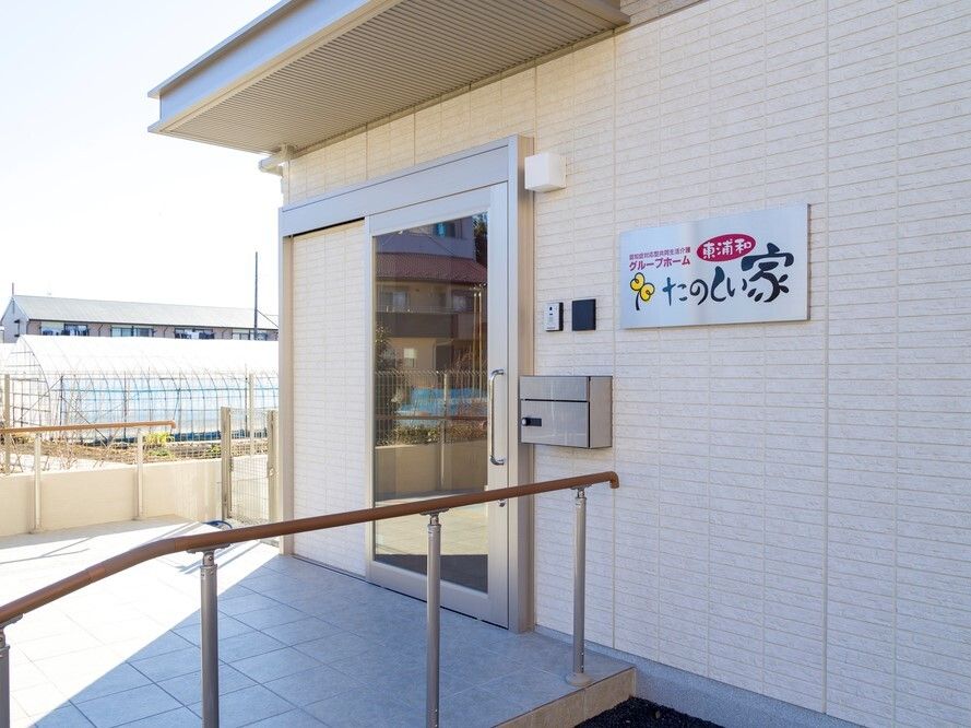 エプロンを付けた若い男女のスタッフに付き添われて屋外で何かを観戦している車いすの高齢の男女。