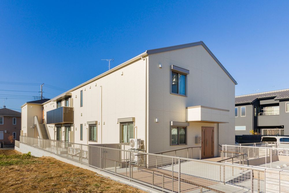 アイボリーの外壁の2階建ての建物の玄関には手すり付きのスロープがあり、駐車場も完備されている。