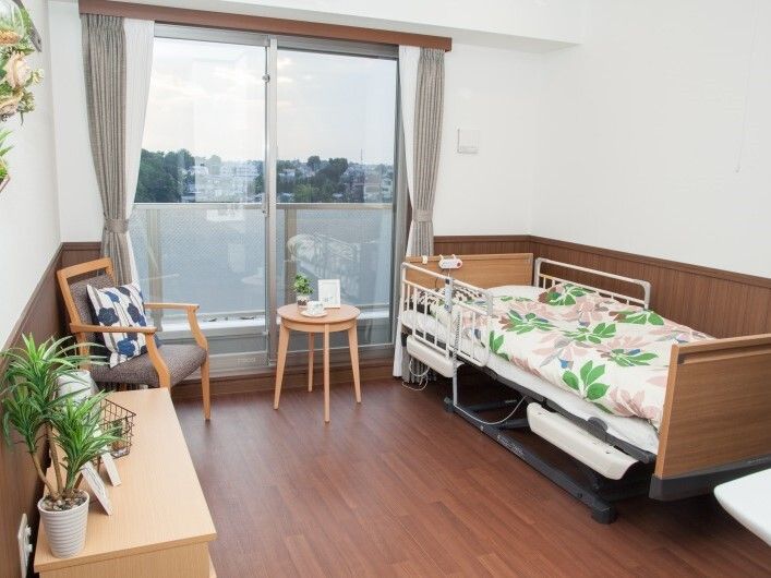 寝具付きのベッドやタンス、ソファが置かれた一人用の椅子などが置かれたフローリングの部屋にはドライフラワーも飾られている。