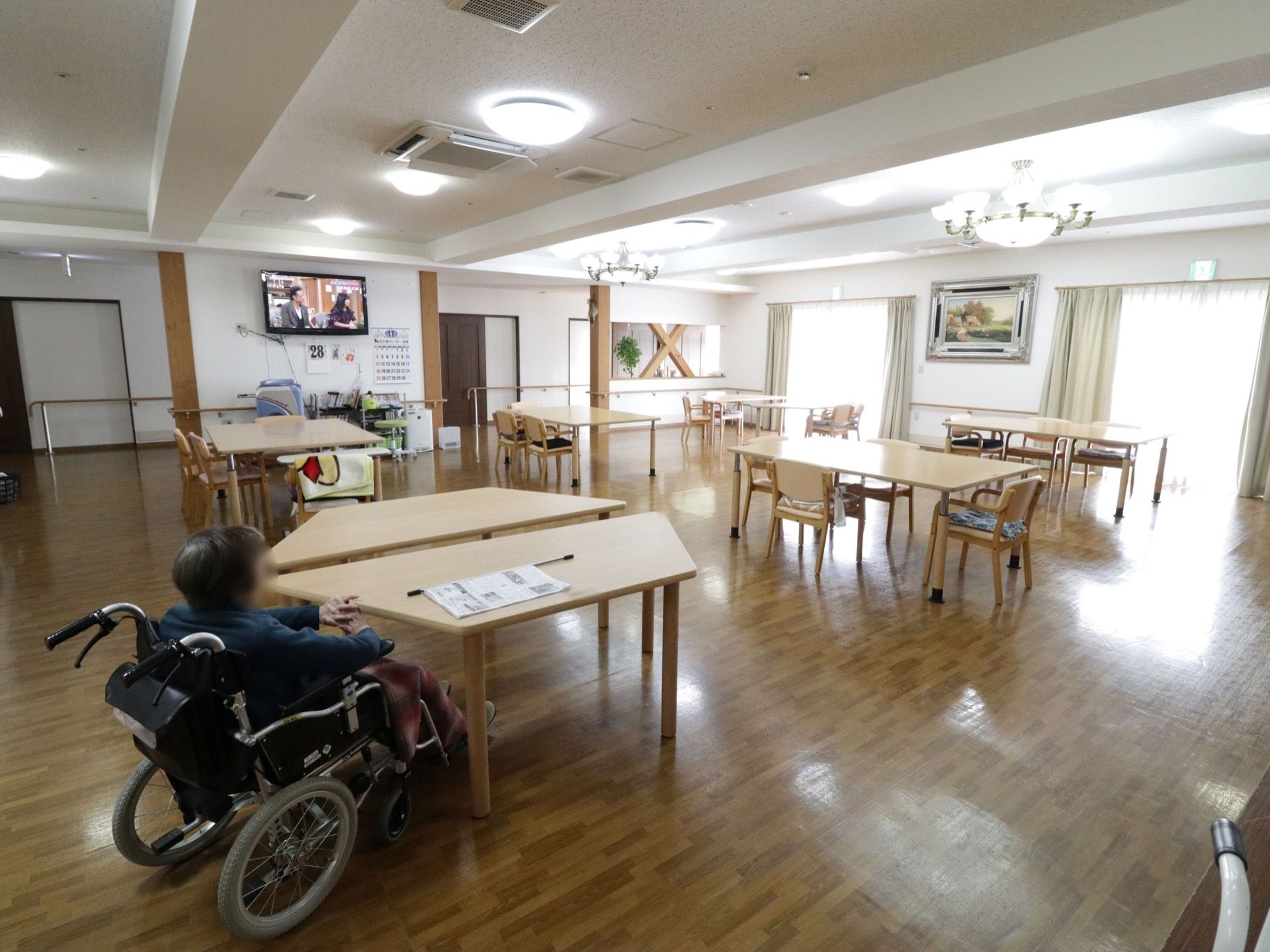 窓から日差しが差しこむ広く明るい食堂である。壁には、絵画やテレビが設置されている。ダイニングテーブルセットが置かれている。