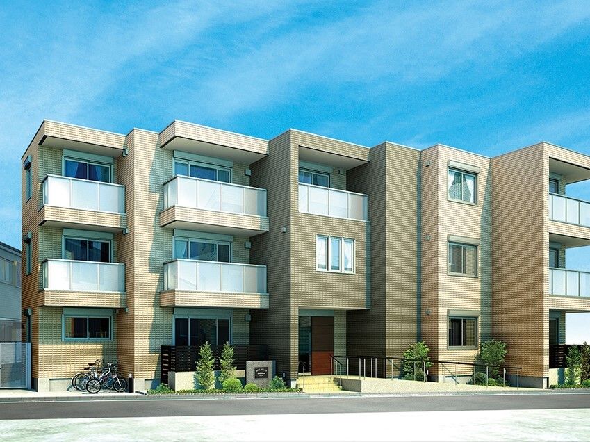 ３階建ての建物はブラウン系で各フロアにベランダがあり、凹凸がある。玄関には手すり付きの階段とスロープが設置されている。